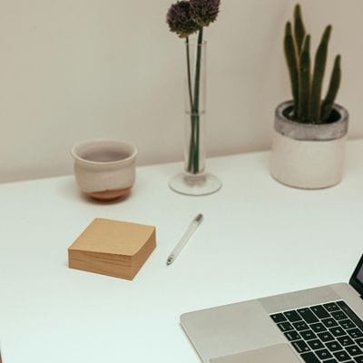 Close up of a corner of a desk showing a laptop, notepad and pen