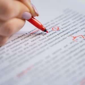 A hand holding a red marker is correcting text on a document, circling errors and adding marks.